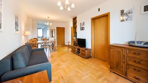 Ein geräumiger Wohnbereich mit einer Couch, Holzschränken, einem Fernseher und einem Essbereich im Hintergrund.