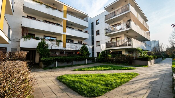 A modern multi-story residential building with balconies, a central courtyard, and surrounding greenery. - Malborska Lovely Apartment (Warszawa)
