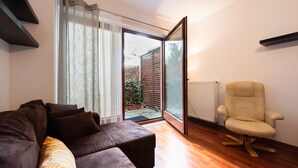 A modern living room with a dark brown sofa, a cream-colored chair, and a sliding glass door leading to a garden. - Malborska Lovely Apartment (Warszawa)