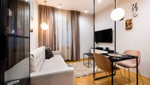 A modern living room with a white sofa, a dining table with chairs, a TV, and a large window with curtains. - Mostowa Abdank Old Town Apartment (Warszawa)