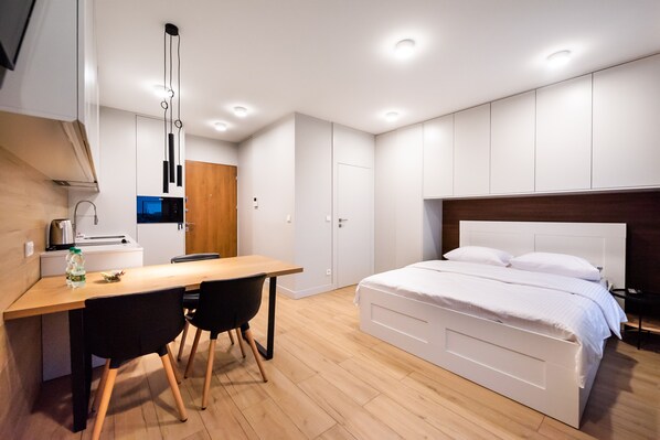 A modern bedroom with a wooden floor, a white bed, and a desk with two chairs. - 7th Floor Atelier Praga Studio (Warszawa)