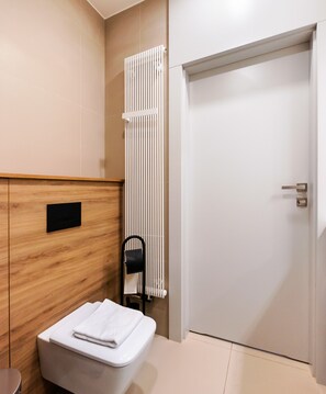 A modern bathroom with a wooden vanity, a white toilet, a towel, and a radiator. - 7th Floor Atelier Praga Studio (Warszawa)