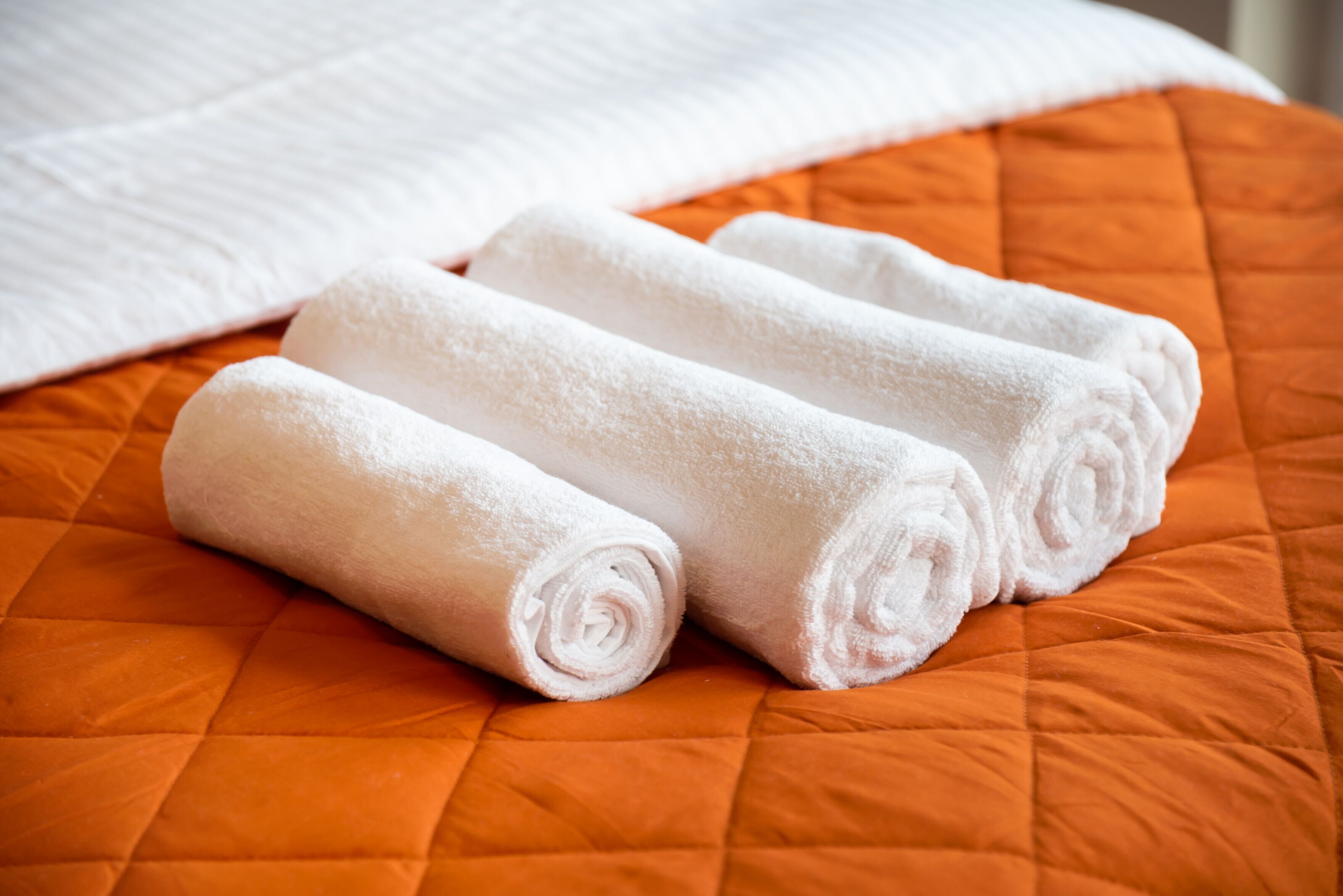 Un lit recouvert d’une couette orange et sur lequel sont posés trois serviettes blanches, soigneusement pliées.