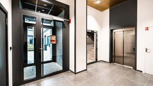 A modern elevator with a metallic finish, a glass door entrance, and a visible emergency exit sign.