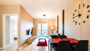 A modern living room with a dining area, a TV, and a large wall clock.