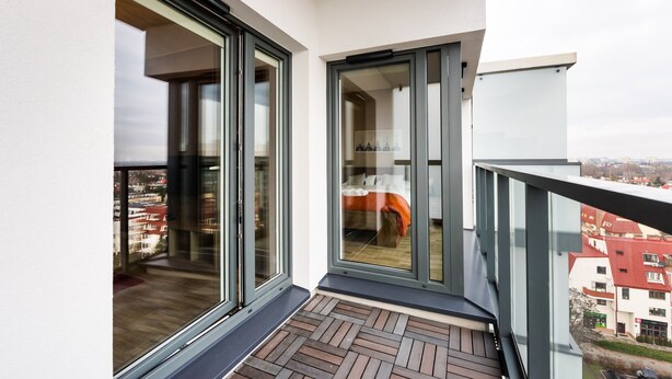 A balcony with a view of the city, a sliding glass door, and a wooden floor.