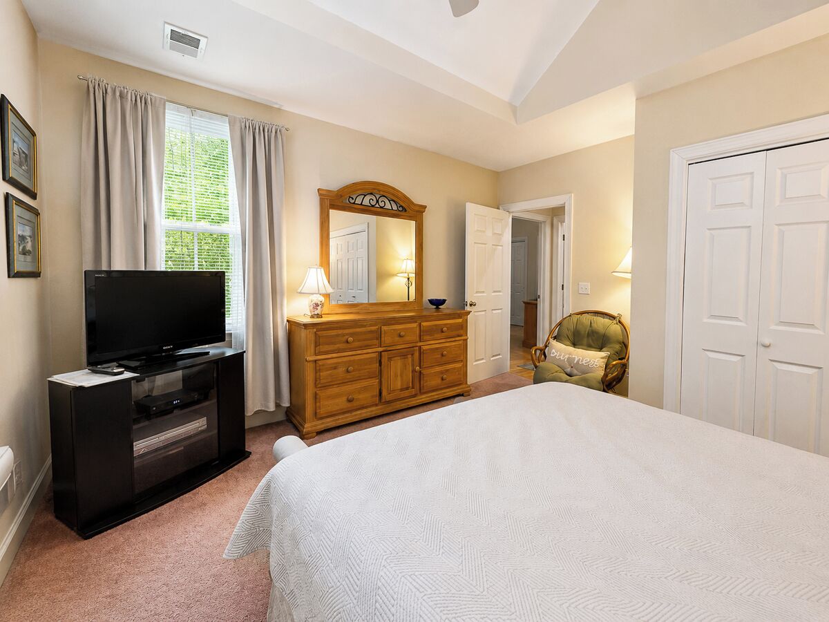 A bedroom with a bed, a dresser, a television, a mirror, and a chair.