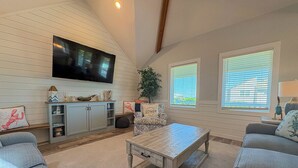 A living room with a TV, sofa, coffee table, and a plant. - Another Day Of Sun - Oceanside 4 BR home w/Hot Tub - 500 feet to beach access (Duck)