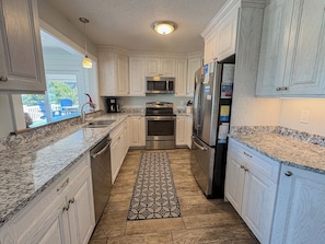 A kitchen with white cabinetry, stainless steel appliances, a patterned rug, and a view of the outside.
