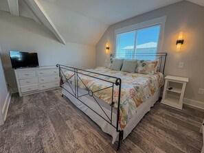 Een slaapkamer met een bed, een kast, een televisie en een raam met jaloezieën.