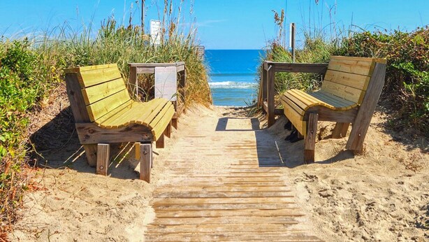 A wooden pathway leading to two wooden benches on a sandy beach with a clear view of the ocean. - Another Day Of Sun - Oceanside 4 BR home w/Hot Tub - 500 feet to beach access (Duck)