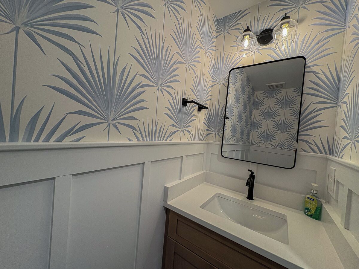 A bathroom with a white sink, a mirror, and a wall with a palm leaf pattern.