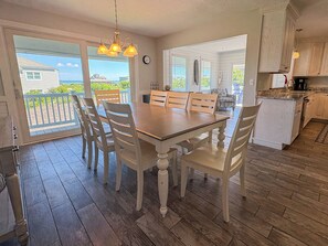 Een eethoek met een houten tafel en stoelen, een keuken op de achtergrond en uitzicht op de oceaan door een schuifdeur.