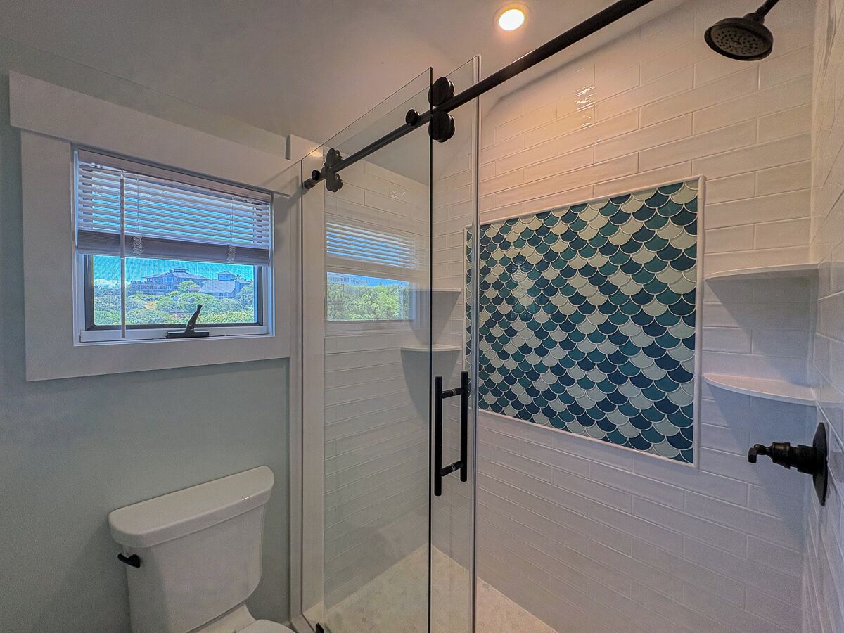 A glass-enclosed shower with a window, a white toilet, and a tiled wall with a blue pattern.