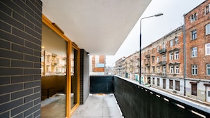 Een smal balkon met een glazen deur naar een kamer, met uitzicht op een straat met klassieke bakstenen panden.