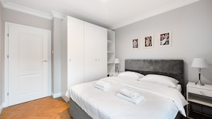 Een moderne slaapkamer met een groot bed, een witte kledingkast en een nachtkastje met een lamp.