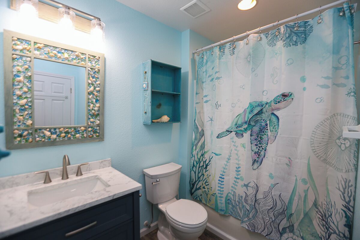 A bathroom with a sea turtle shower curtain, a sink with a marble countertop, and a toilet.