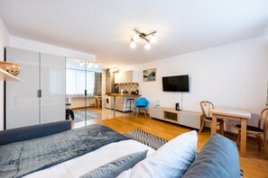 A modern bedroom with a large bed, a desk, and a kitchenette in the background. - Plac Grzybowski Blue Sky Studio (Warszawa)