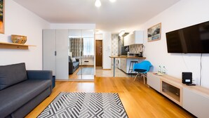 Una sala de estar moderna con un sofá gris, un alfombra estampado y una zona de cocina con una silla azul y un televisor.