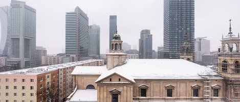 A historic building with a snow-covered roof, surrounded by modern high-rise buildings.