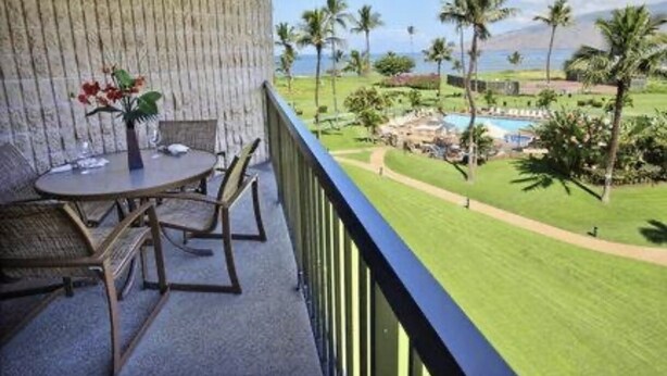 A balcony with a table and chairs, overlooking a pool and lush greenery.