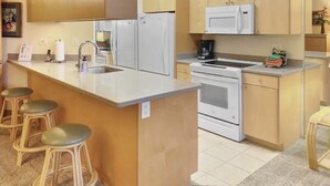A kitchen with a central island, bar stools, a microwave, a stove, and wooden cabinets.
