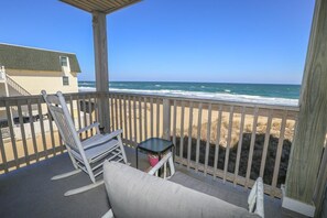 Ein Balkon mit Blick auf den Strand, ein Schaukelstuhl, ein kleiner Tisch und ein Kissen.