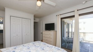 Una camera da letto con un letto, una cassettiera, una televisione e una porta scorrevole in vetro che dà su un balcone.