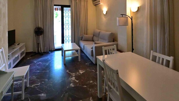 Una sala de estar con sofá, mesa de comedor, televisor y ventilador.