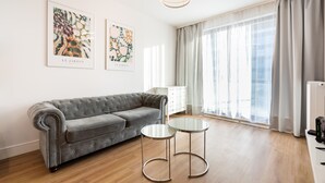 A modern living room with a grey sofa, two small round tables, and artwork on the wall. - Wola Bloom Apartment (Warszawa)