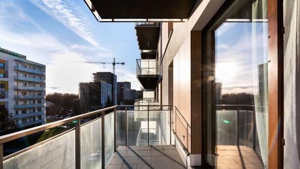 A modern balcony with glass railings, a view of the cityscape, and a construction crane in the background. - Wola Bloom Apartment (Warszawa)