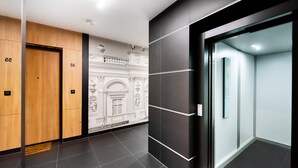 A modern hotel lobby with wooden and black walls, a marble wall with a classical design, and a glass elevator. - Wola Bloom Apartment (Warszawa)