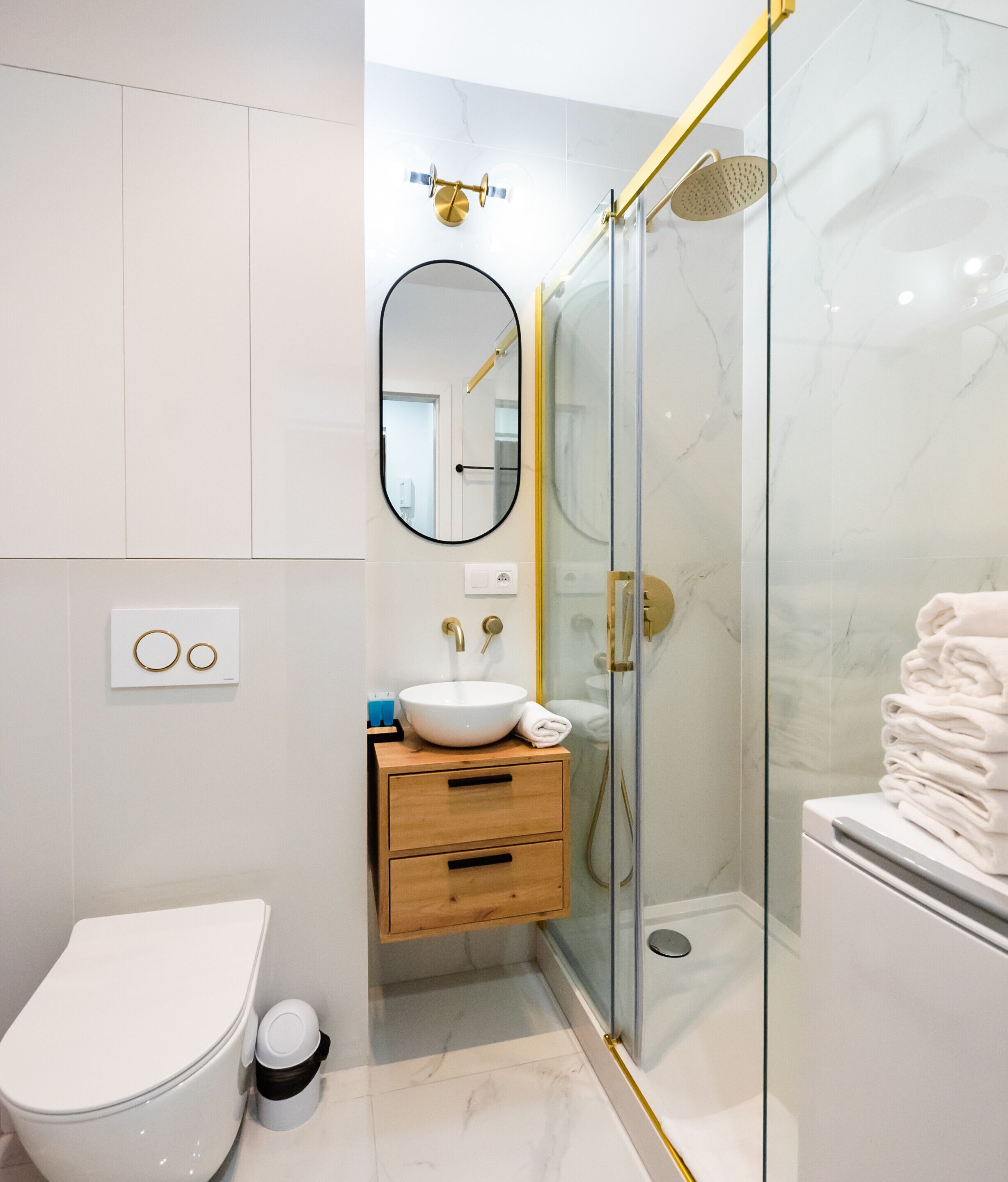 Un baño moderno con cabina de ducha de vidrio, inodoro blanco, tocador de madera con lavamanos y un espejo.