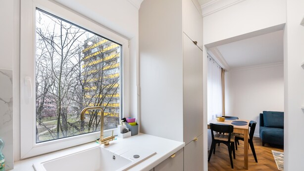 A modern kitchen with a large window, a sink, and a dining area with a table and chairs.