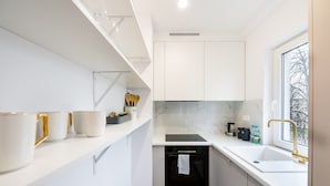 A modern kitchen with white cabinetry, a built-in oven, a sink with a gold faucet, and a window providing a view of the outside.