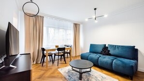 A modern living room with a blue sofa, a round coffee table, a TV, and a dining area with a table and chairs.