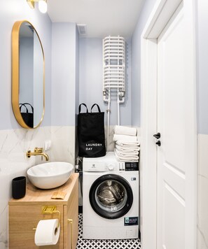 Ein kleines Badezimmer mit Waschbecken, Spiegel, Handtuchhalter und einer Waschmaschine.