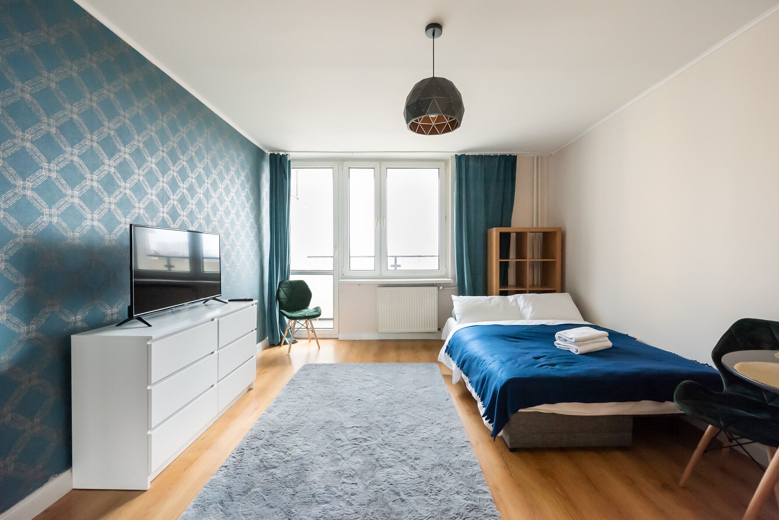 A modern bedroom with a bed, a TV, a dresser, and a window with curtains.