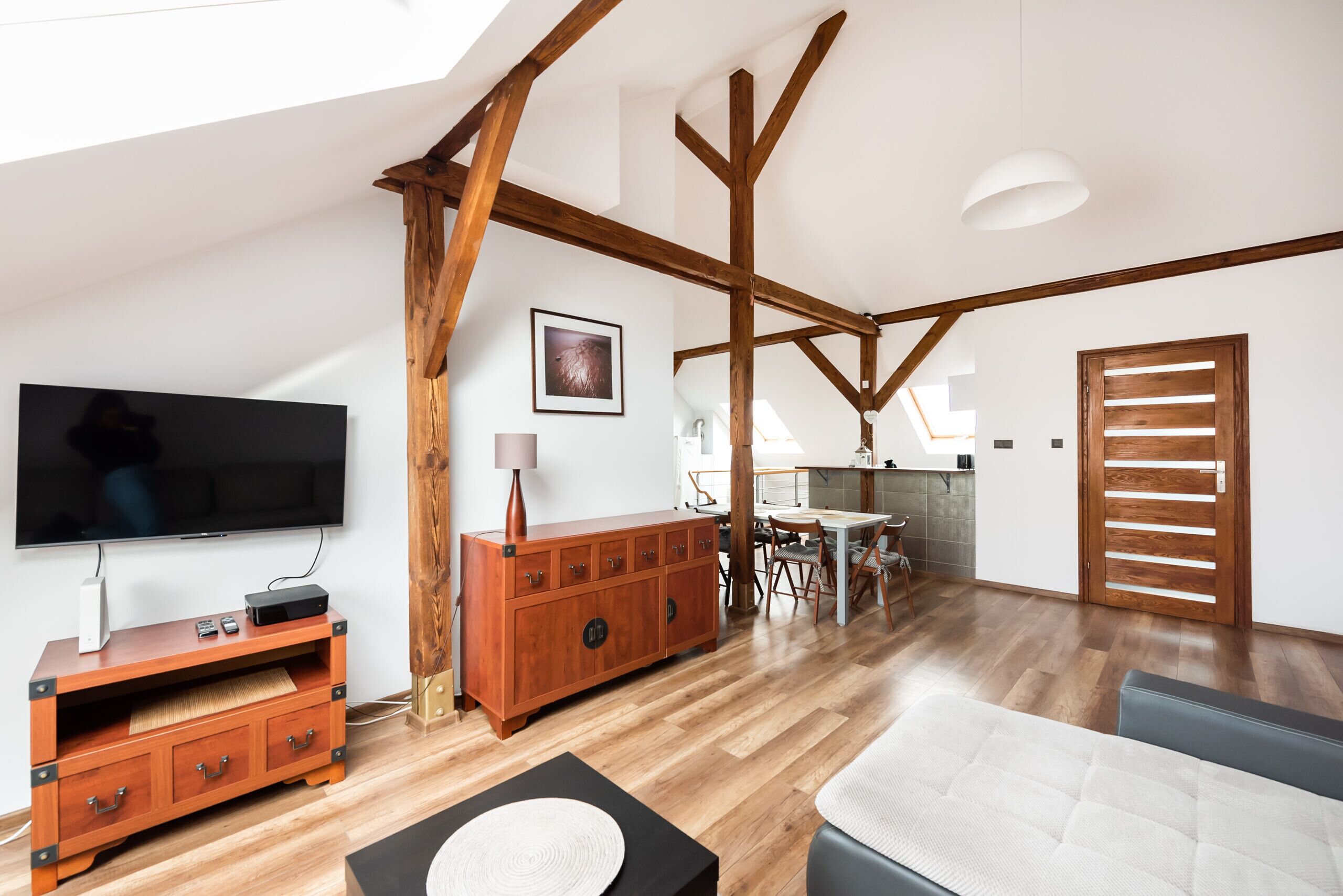 A spacious living area with a wooden ceiling, a flat-screen TV, a wooden cabinet, and a dining area with a table and chairs.