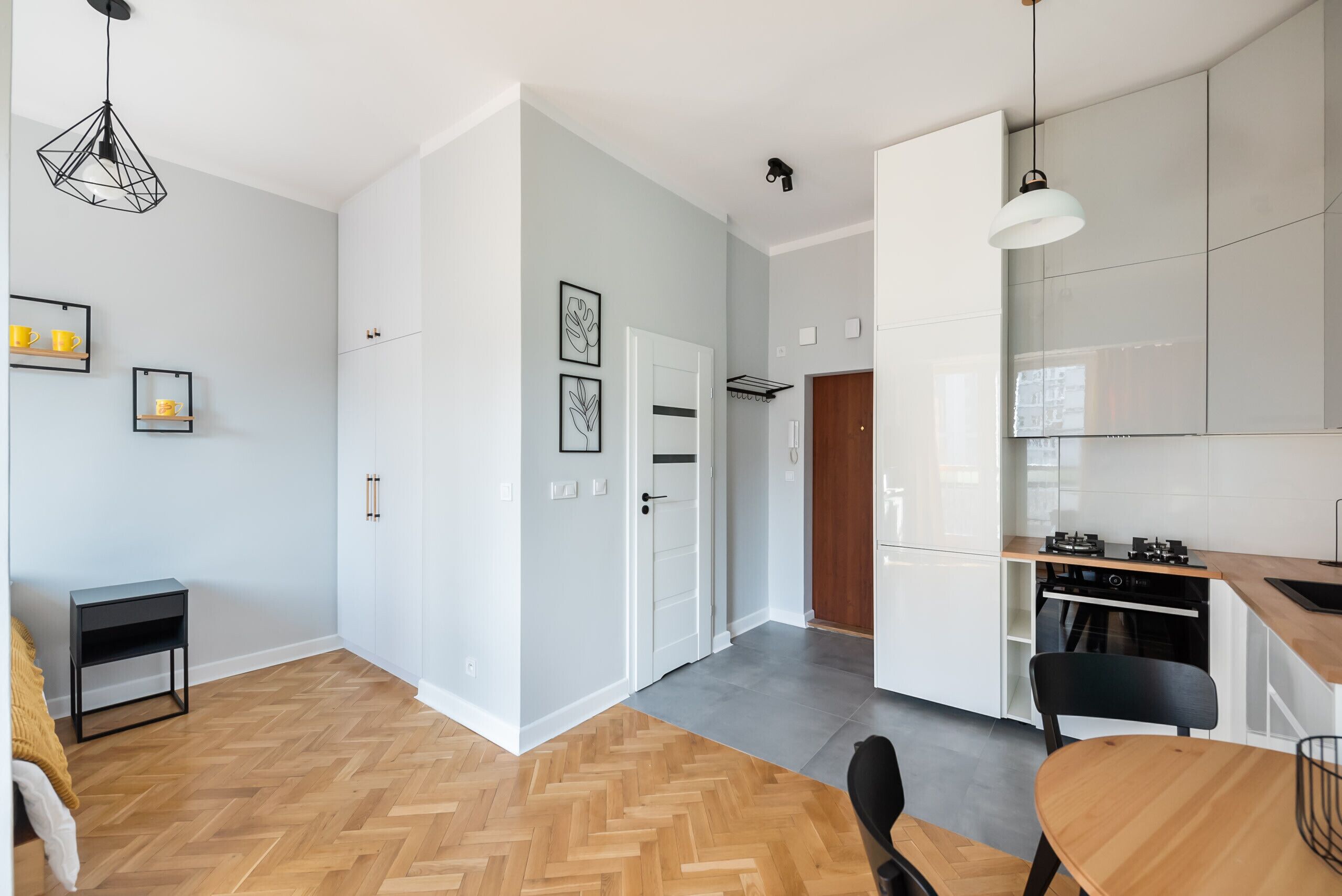 A modern kitchen with white cabinets, a wooden dining table, and a herringbone floor pattern.