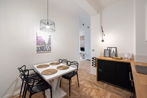 A modern kitchen with a wooden countertop, a black cabinet, and a dining area with a white table and black chairs. - Old Town Basilisk Apartment (Warszawa)