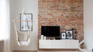 A modern living room with a brick wall, a hanging chair, a white console table with a flat-screen TV, and framed pictures. - Old Town Basilisk Apartment (Warszawa)