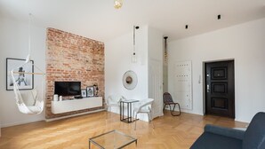 A living room with a brick wall, white furniture, a hanging chair, and a TV. - Old Town Basilisk Apartment (Warszawa)