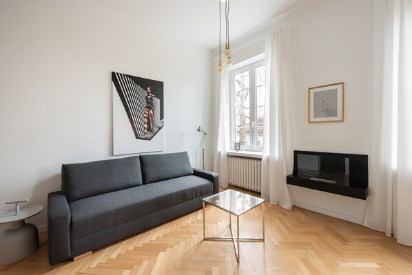 A modern living room with a grey sofa, a glass coffee table, a mounted TV, and a large window with curtains. - Old Town Basilisk Apartment (Warszawa)
