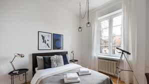 A bedroom with a bed, a window with curtains, a standing lamp, and a telescope. - Old Town Basilisk Apartment (Warszawa)