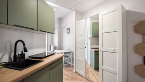 Een moderne keuken met een houten aanrecht, een zwarte spoelbak en groene kastjes. Er is een witte deur die naar een andere kamer leidt en een kleine tafel met een stoel op de achtergrond.