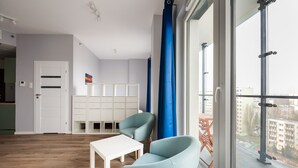 Een moderne woonkamer met een witte tafel, twee lichtblauwe stoelen, een wit kastje en een groot raam met uitzicht op gebouwen.