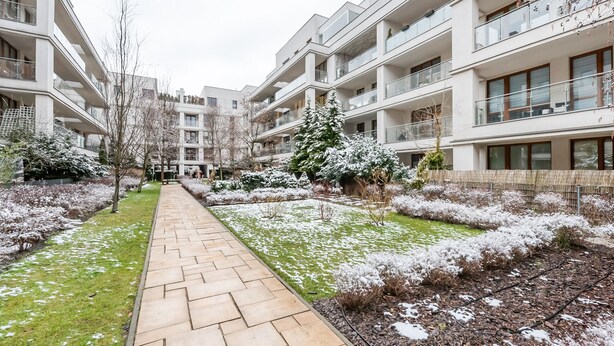 Ein modernes Wohngebäude mit mehreren Balkonen, einem zentralen Weg und schneebedeckter Bepflanzung.