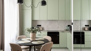 A modern kitchen with green cabinets, a round dining table with four chairs, and pendant lights. - Plac Politechniki Pistachio Apartment (Warszawa)