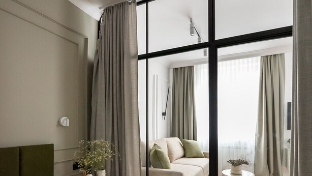 A modern bedroom with a large bed, a nightstand, a vase with flowers, and a view through a glass door to a living area with a sofa and a table. - Plac Politechniki Pistachio Apartment (Warszawa)